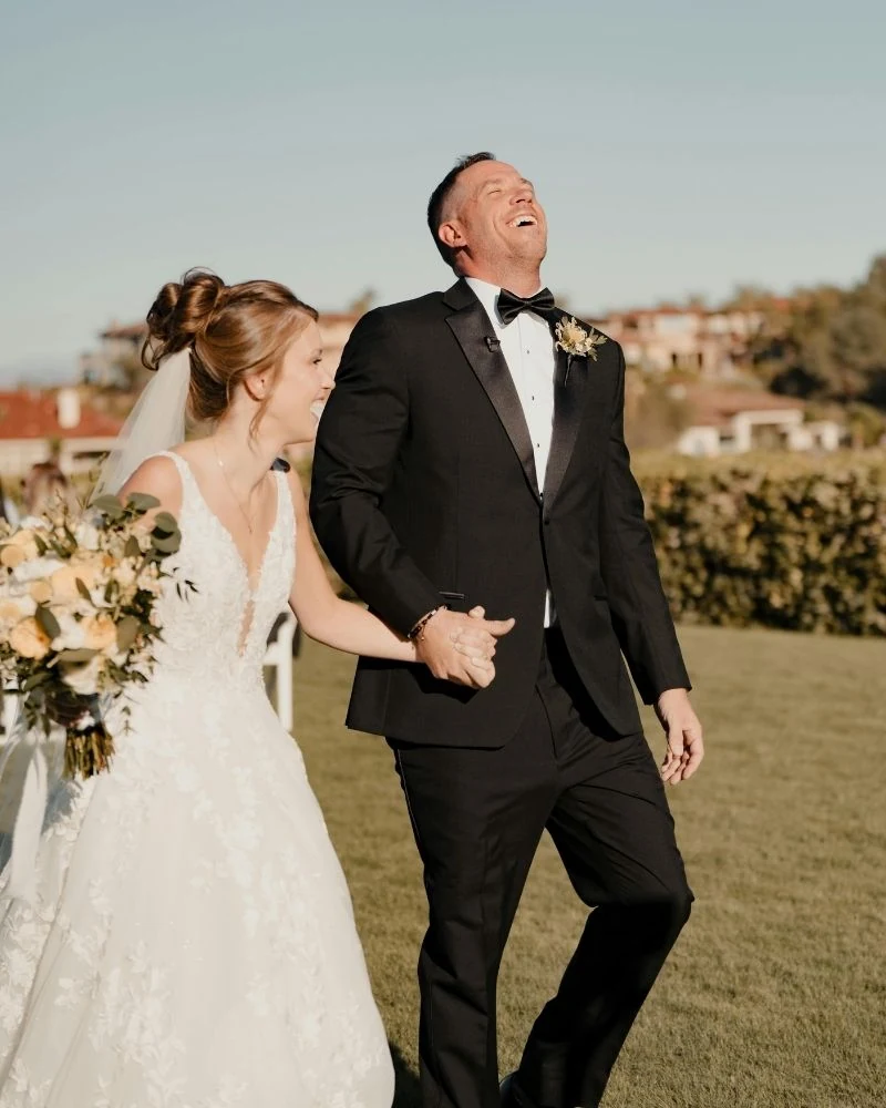 A bride and groom walking hand in hand, laughing, after the ceremony