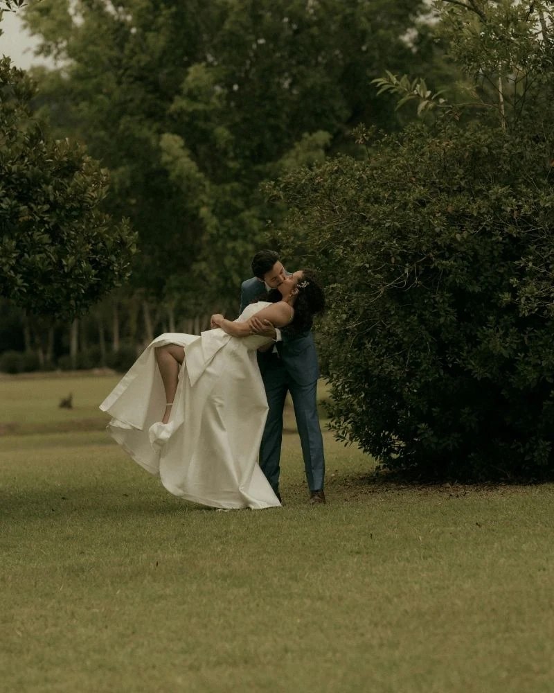 A groom dipping his bride in a garden among trees
