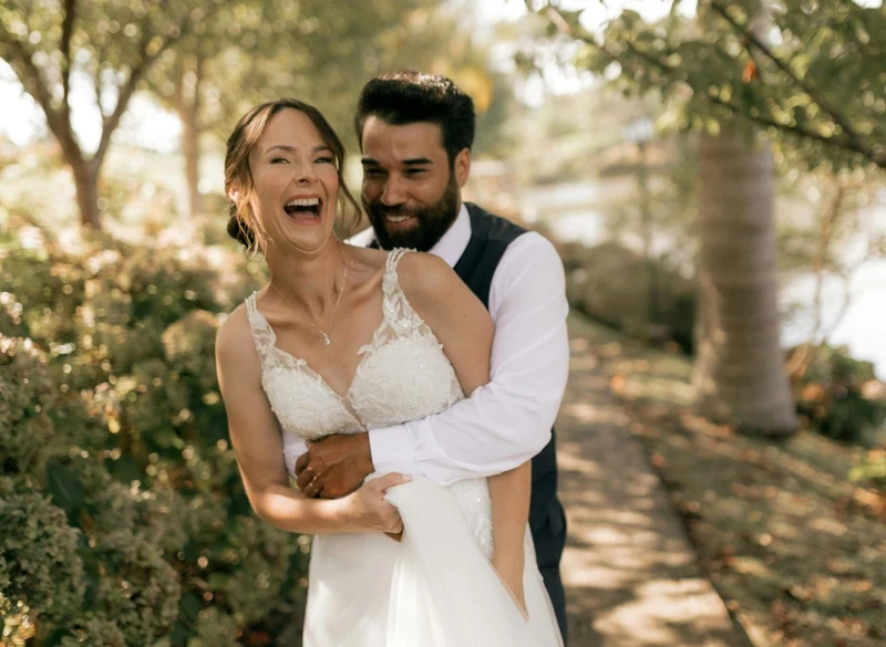 A laughing bride and groom embracing in a sunlit garden